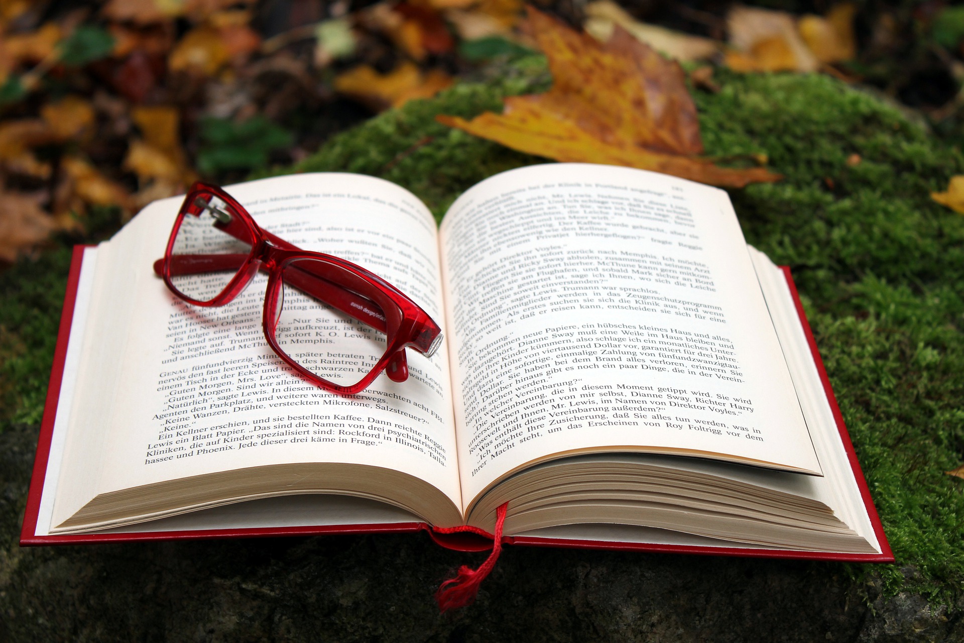 paire de lunettes rouge posée sur un livre ouvert sur fond de feuilles d'automne