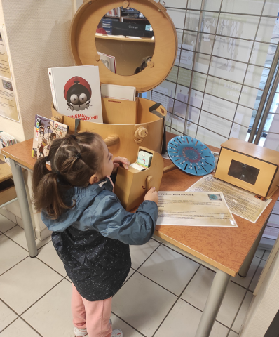petite fille de dos regardant des objets sur une table face à une malle ouverte avec un miroir