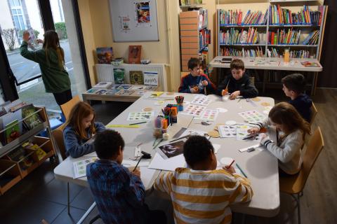 enfants assis autour d'une grande table avec du matériel pour découper