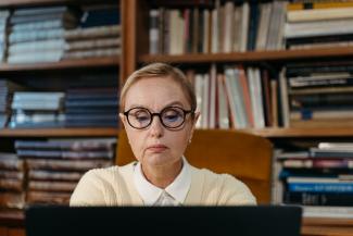 Femme avec un chignon et des lunettes qui travaille sur un ordinateur devant une bibliothèque