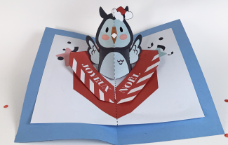 Carte en pop-up représentant une chouette avec un bonnet de Noël sortant d'un cadeau portant l'inscription "Joyeux Noël"