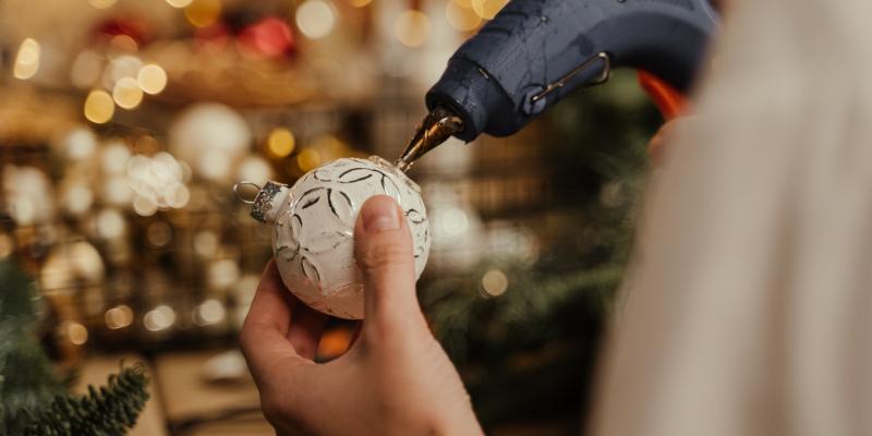 Personne en train de décorer une boule de Noël à l'aide d'un pistolet à colle